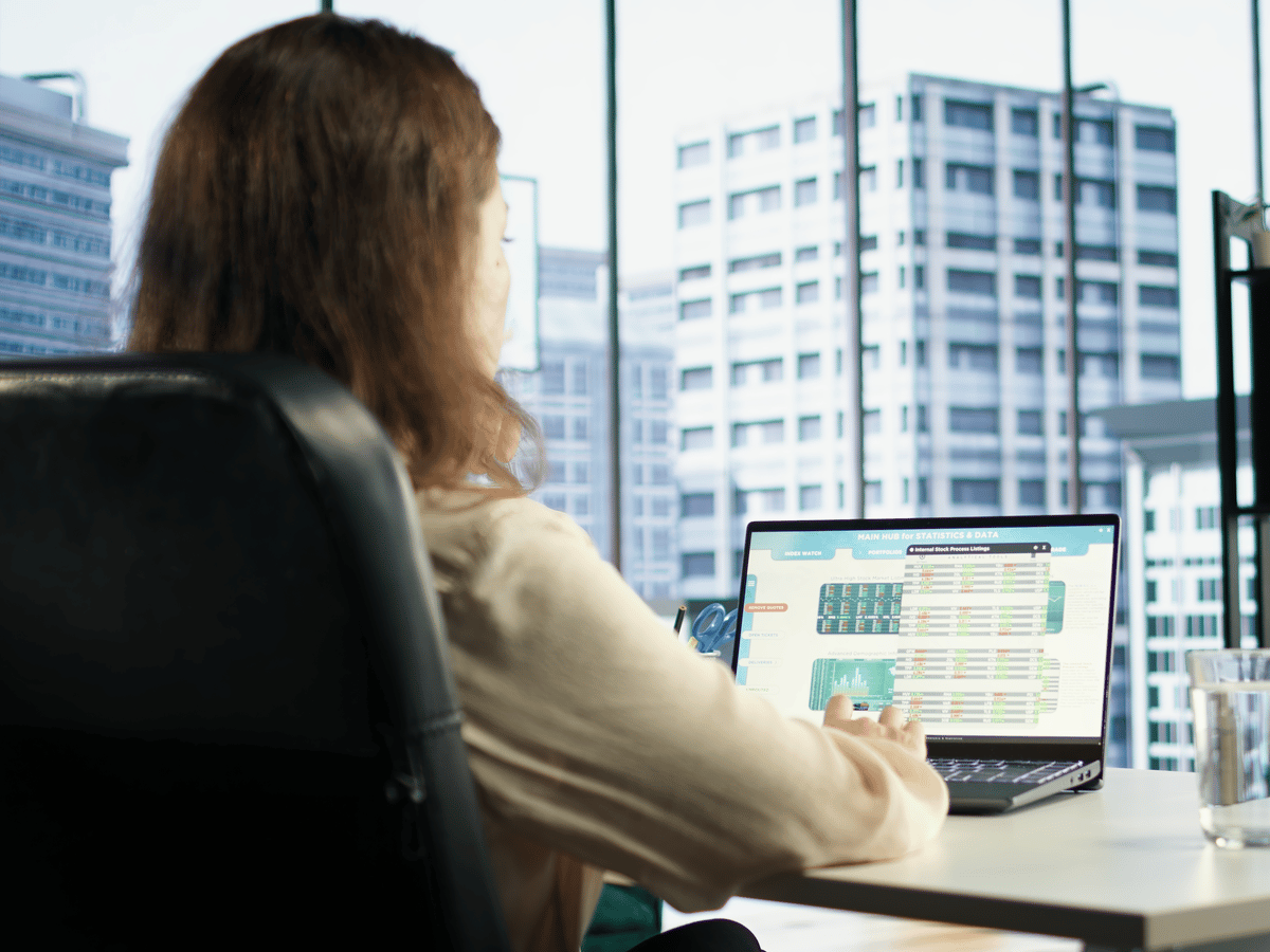 An analyst at a laptop with city office towers outside the window